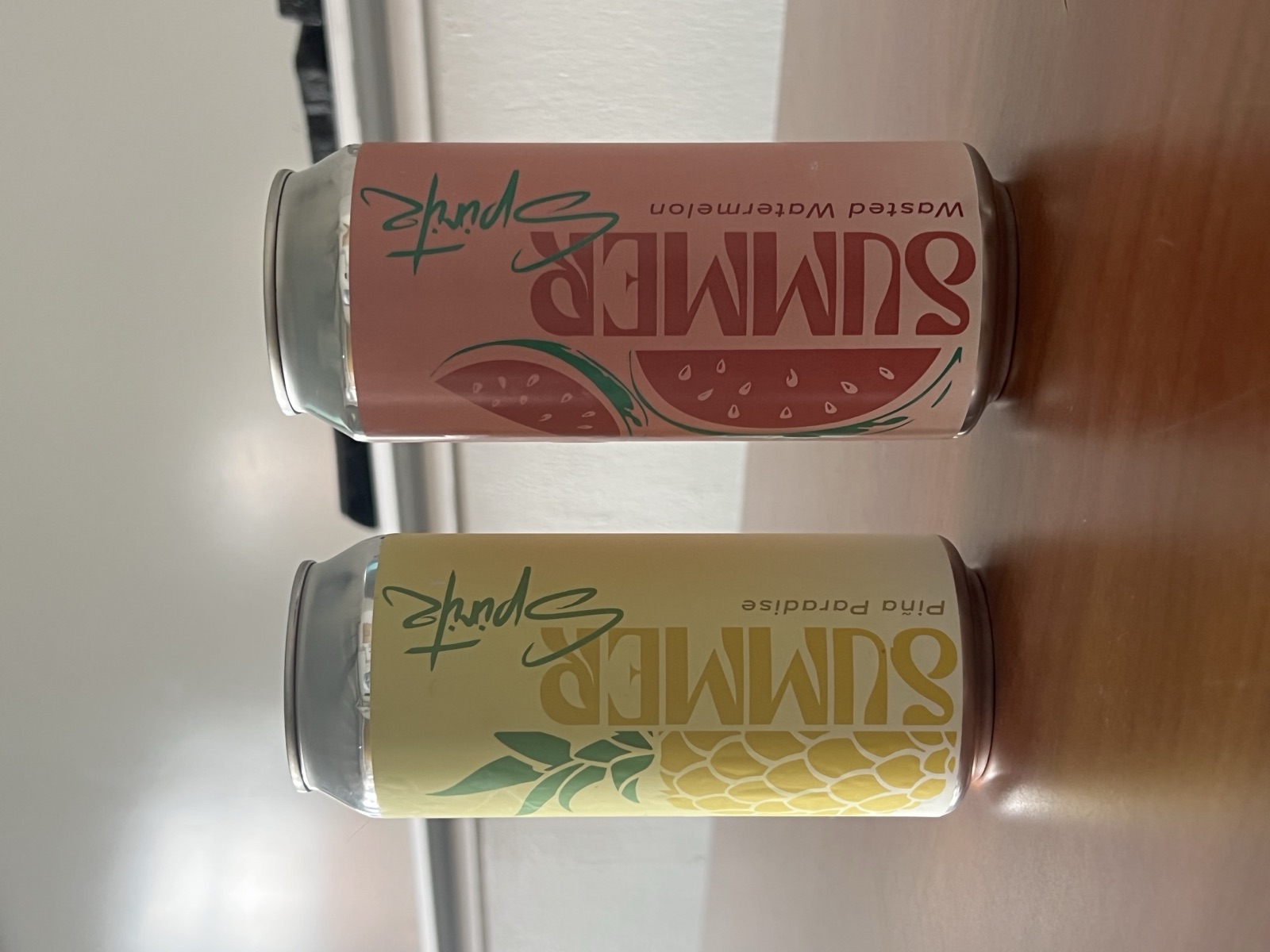 Piña Paradise and Wasted Watermelon printed cans on a table